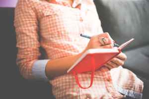 Woman in a checkered shirt writing in a red notebook