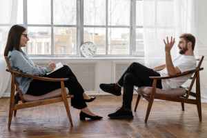 Man and woman sitting across from each other in wooden chairs during a therapy session
